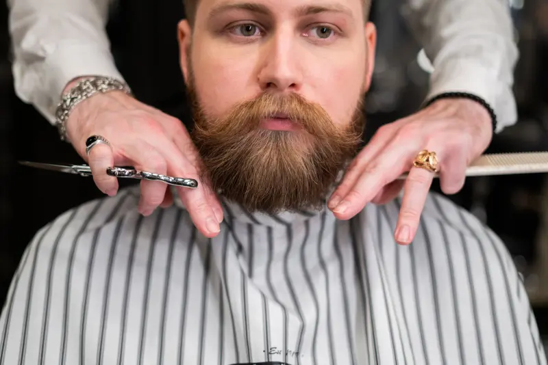 Barbero perfilando con tijera la barba de un cliente