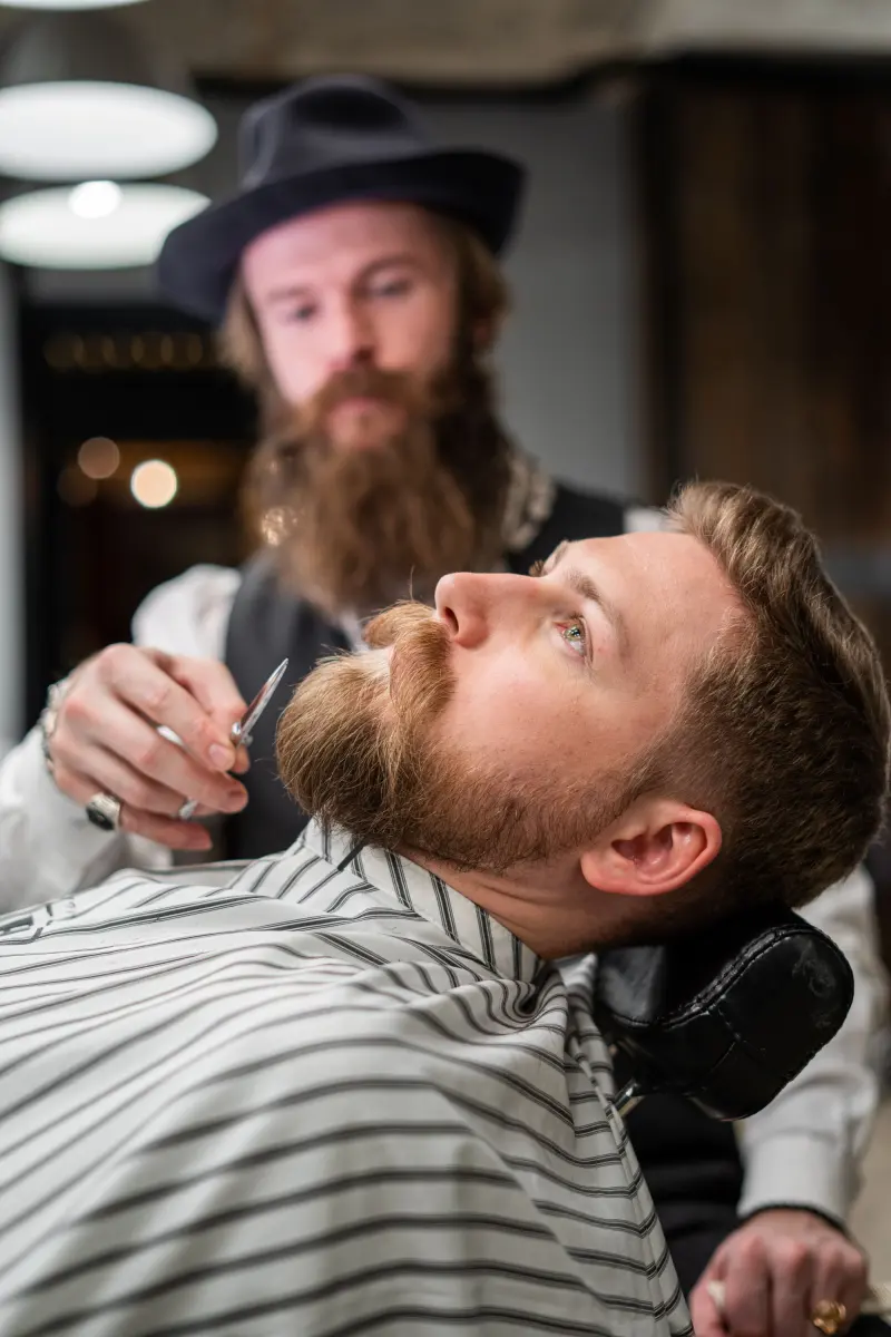 Cliente con barba larga reclinado mientras el barbero la revisa